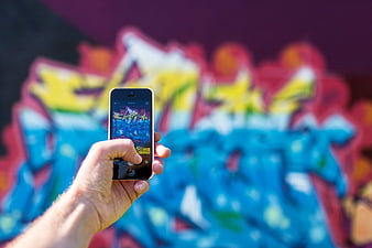 Hand holding smartphone photographing colorful graffiti wall