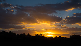 Dramatic sunset with sun rays breaking through clouds over silhouette