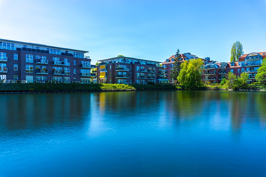 Modern brick apartment buildings along a calm blue lake