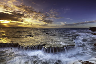 Dramatic Sunset Over Ocean Waterfall with Long Exposure Waves