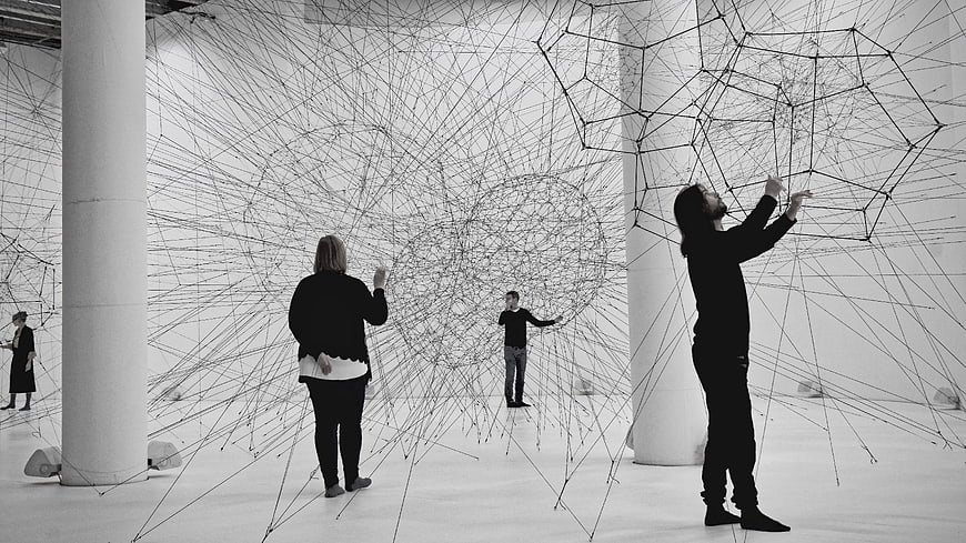 Visitors interacting with large-scale wire network art installation in gallery