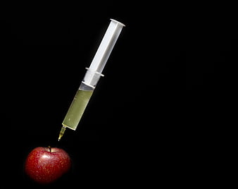 Syringe Injecting Green Liquid Into Red Apple On Black Background