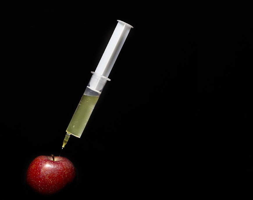 Syringe Injecting Green Liquid Into Red Apple On Black Background