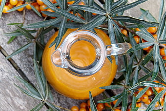 Sea Buckthorn Juice in Glass Pitcher with Fresh Berries and Leaves