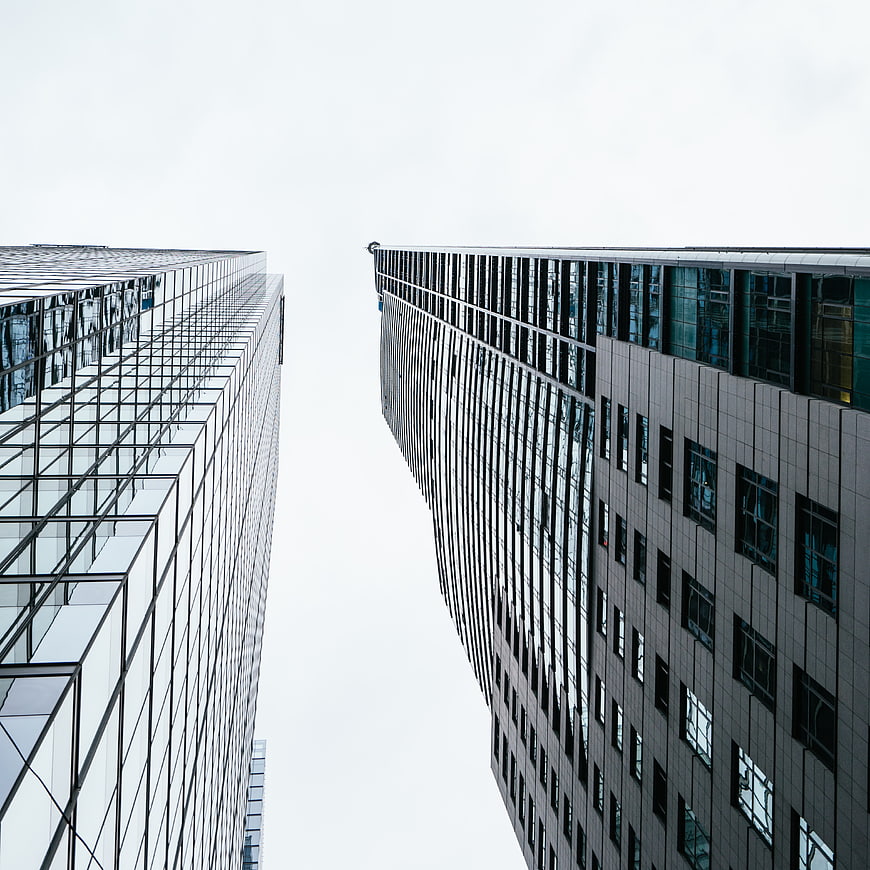 Low angle view of modern glass skyscrapers against white sky