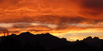 Dramatic orange sunset sky over dark mountain silhouettes