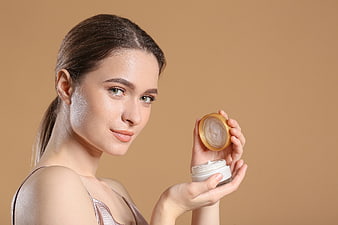 Woman holding skincare cream jar with golden lid