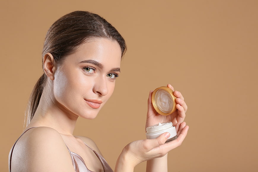 Woman holding skincare cream jar with golden lid