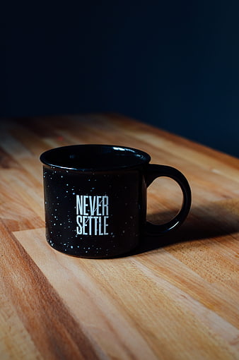Black enamel mug with Never Settle quote on wooden table
