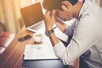 Stressed Businessman Holding Head at Desk with Laptop