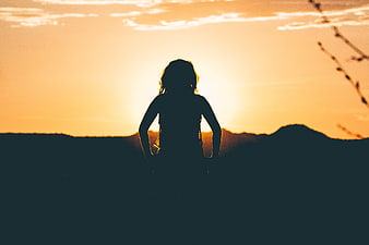 Silhouette of Woman Standing Against Golden Sunset Sky