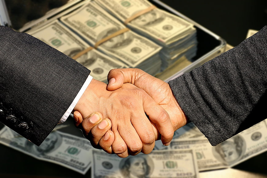 Business handshake over stacks of US dollar bills in briefcase