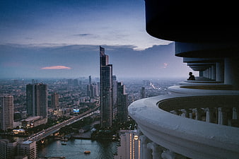 Silhouette of man on balcony overlooking city skyline at dusk