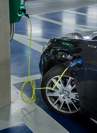 Black electric car charging with yellow cable in parking garage