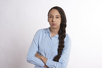 Serious young woman with long braid and crossed arms in blue shirt