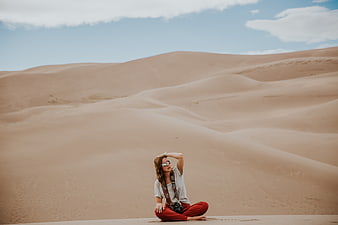 Woman in Red Pants Sitting on Sand Dunes in Desert