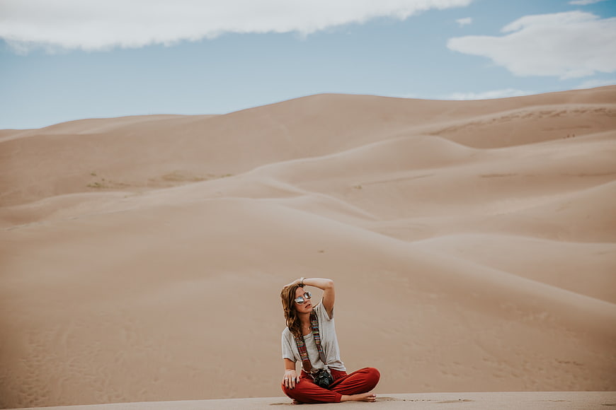 Woman in Red Pants Sitting on Sand Dunes in Desert