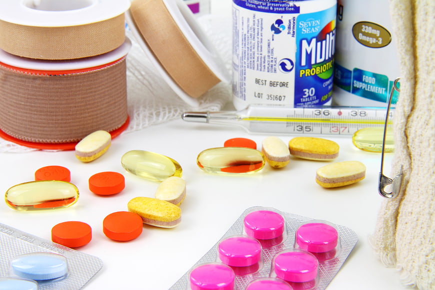 First aid kit with pills, bandages, and thermometer on white background
