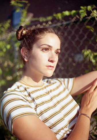 Young woman in striped shirt leaning against chain-link fence outdoors