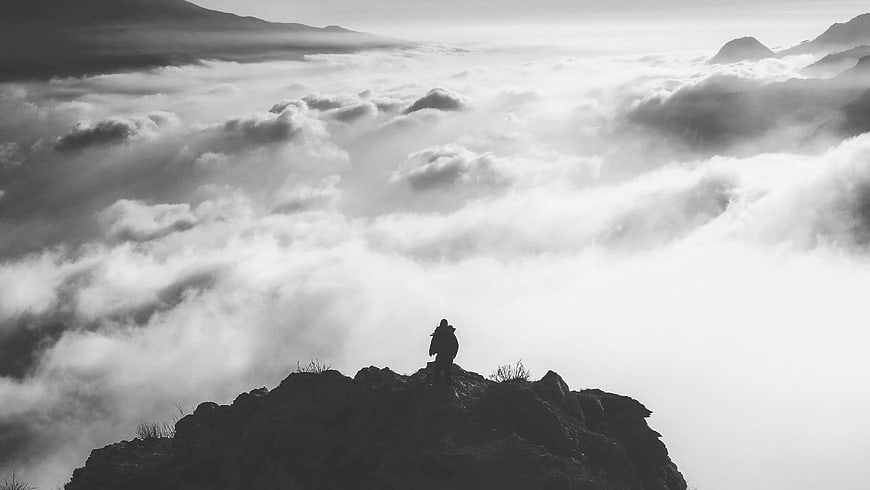 Silhouette of hiker on mountain peak above sea of clouds