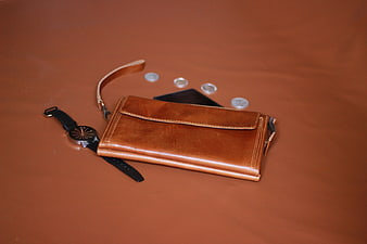 Brown leather pouch with watch and coins on brown background