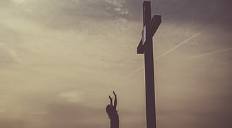 Silhouette of Woman Praying Before Large Cross at Sunset