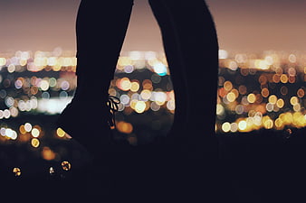 Silhouette of legs dangling over city bokeh lights at night
