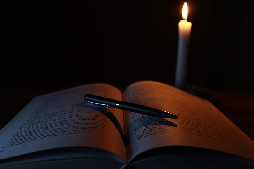 Open book with pen and candle in dark setting