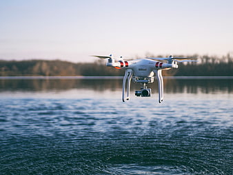 White drone hovering over calm lake water