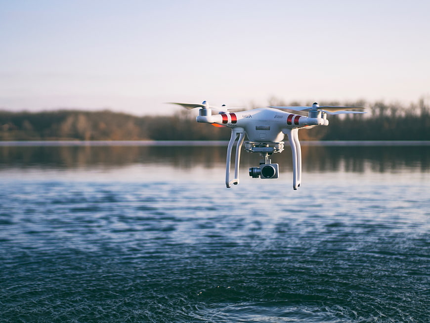 White drone hovering over calm lake water