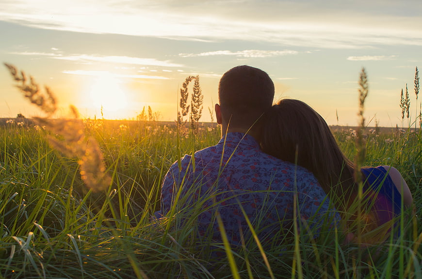 Couple sitting in grassy field watching sunset