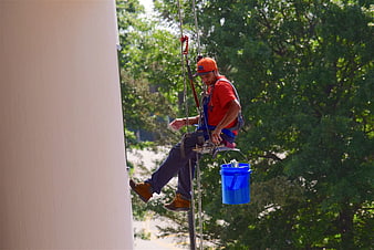 Window cleaner working on a building exterior with safety harness and blue bucket