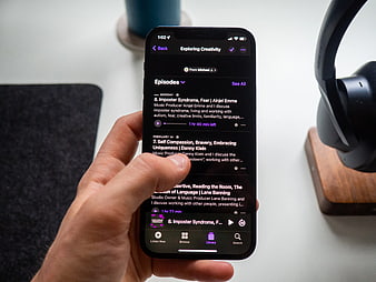 Hand Holding Smartphone Playing Podcast on Desk