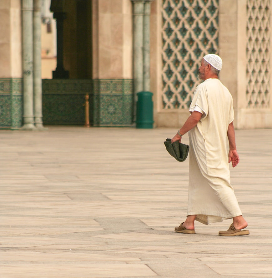 Muslim man walking in traditional white robe at Moroccan mosque courtyard