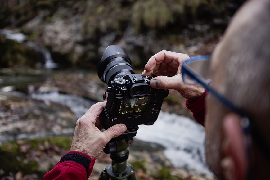 Photographer adjusting camera settings by a stream
