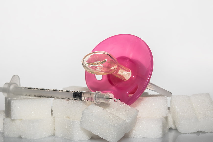 Pink Baby Pacifier, Insulin Syringe, And Sugar Cubes On White Background