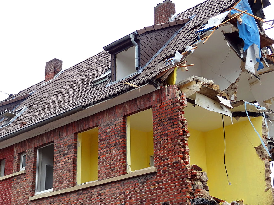 Partially Demolished Brick House With Exposed Yellow Walls And Roof Damage