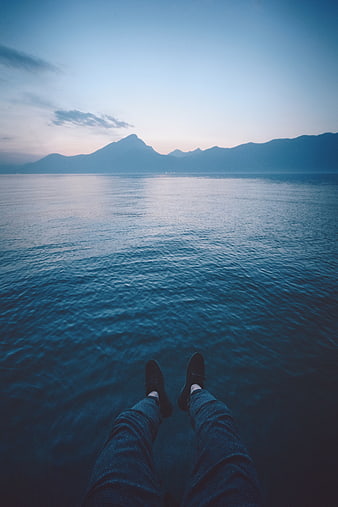 First Person View of Legs Dangling Over Calm Sea at Dusk