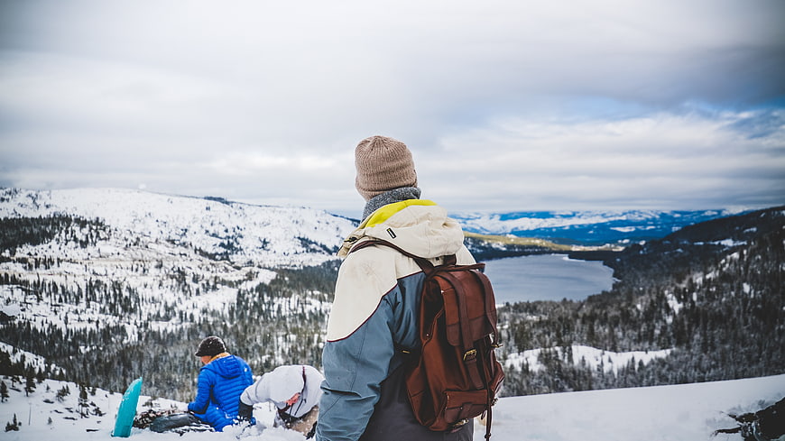 Hikers overlooking snowy mountain valley with frozen lake