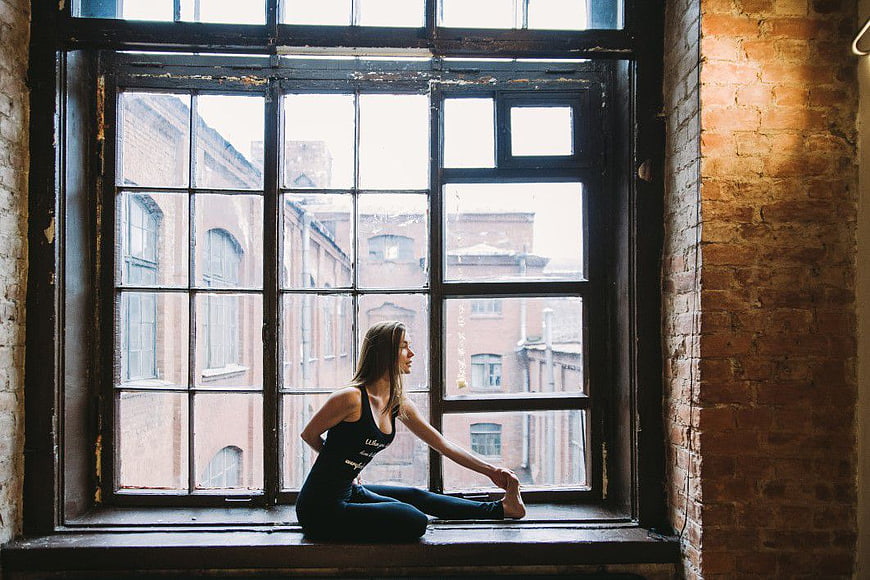 Woman Stretching in Yoga Pose by Large Industrial Window