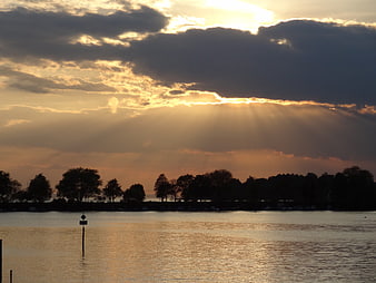 Dramatic sunset sunbeams over a calm lake with silhouetted trees
