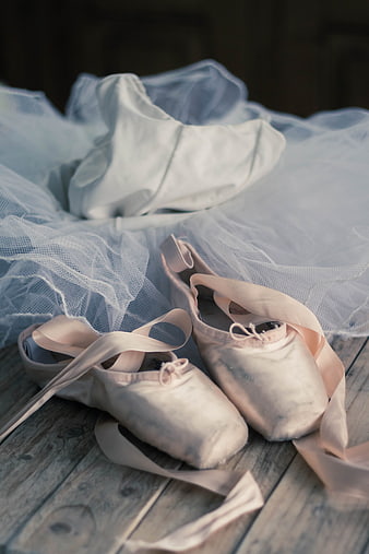 Worn pink ballet pointe shoes and white tutu on wooden floor