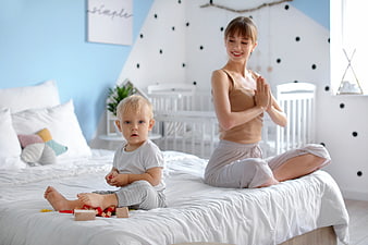 Mother doing yoga on bed with toddler playing