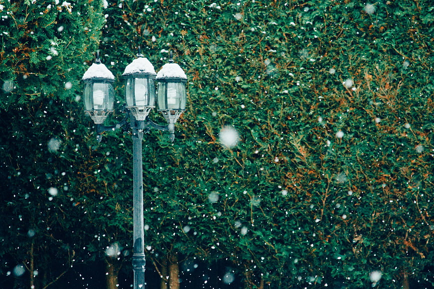Vintage street lamp in snowfall against green hedge