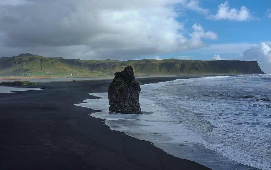 Dramatic black sand beach with sea stack and green cliffs