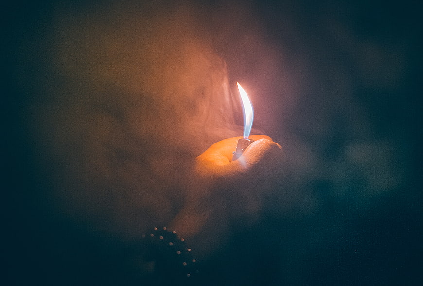 Hand holding a lit candle in dark smoky atmosphere