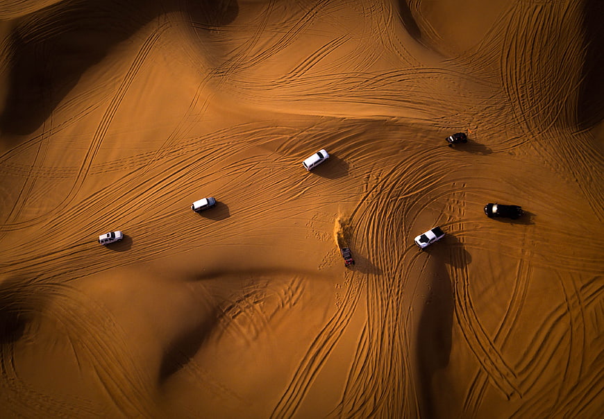 Aerial view of off-road cars driving on golden desert dunes