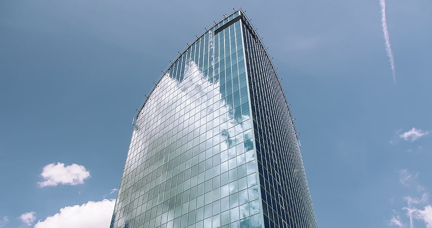 Modern Glass Skyscraper Reflecting Clouds Against Blue Sky