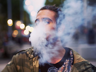 Man exhaling thick smoke outdoors at night with city bokeh