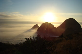Sunset over foggy ocean with silhouetted coastal rock formations